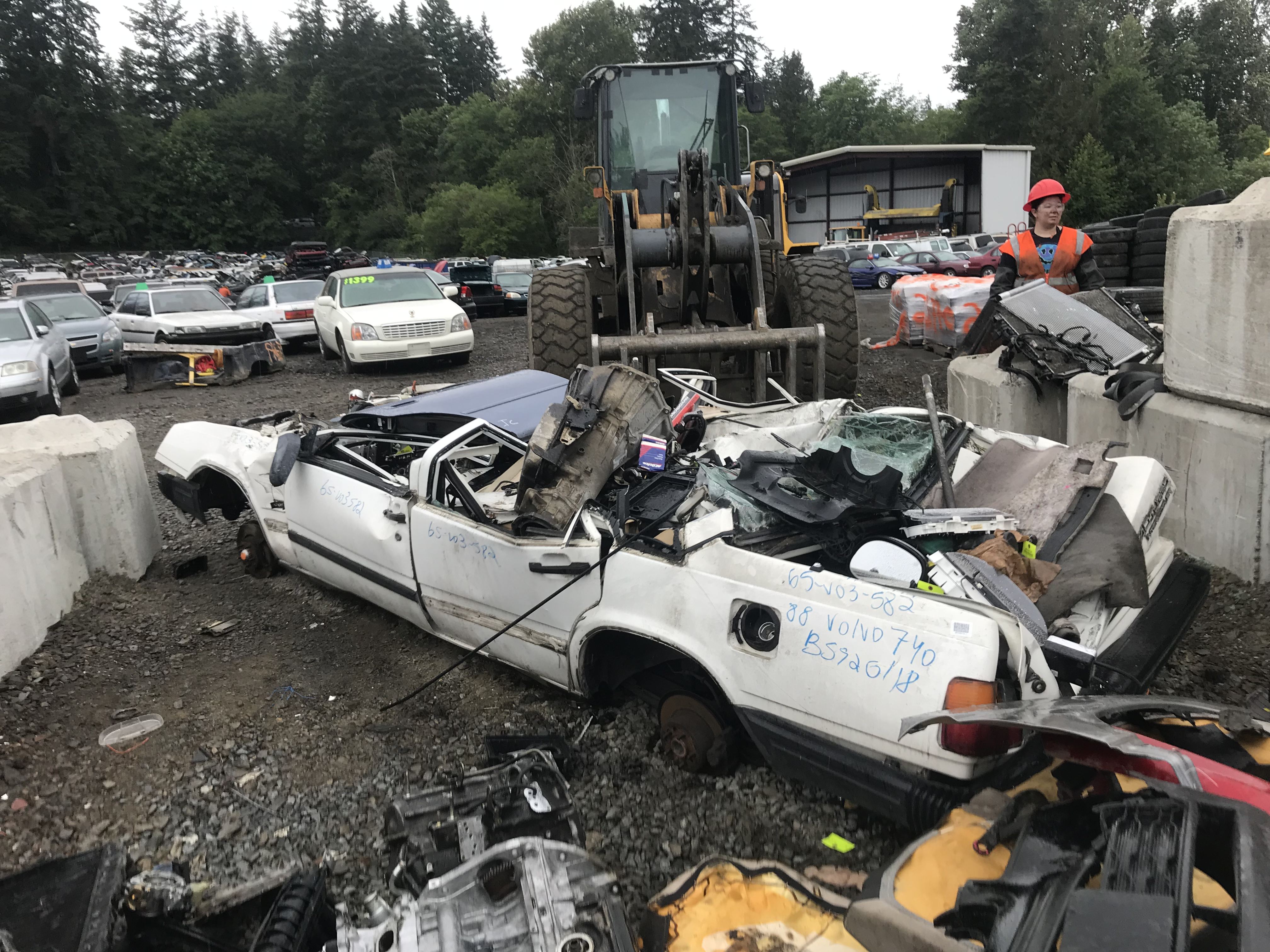 A crushed white car filled with trash in a junkyard