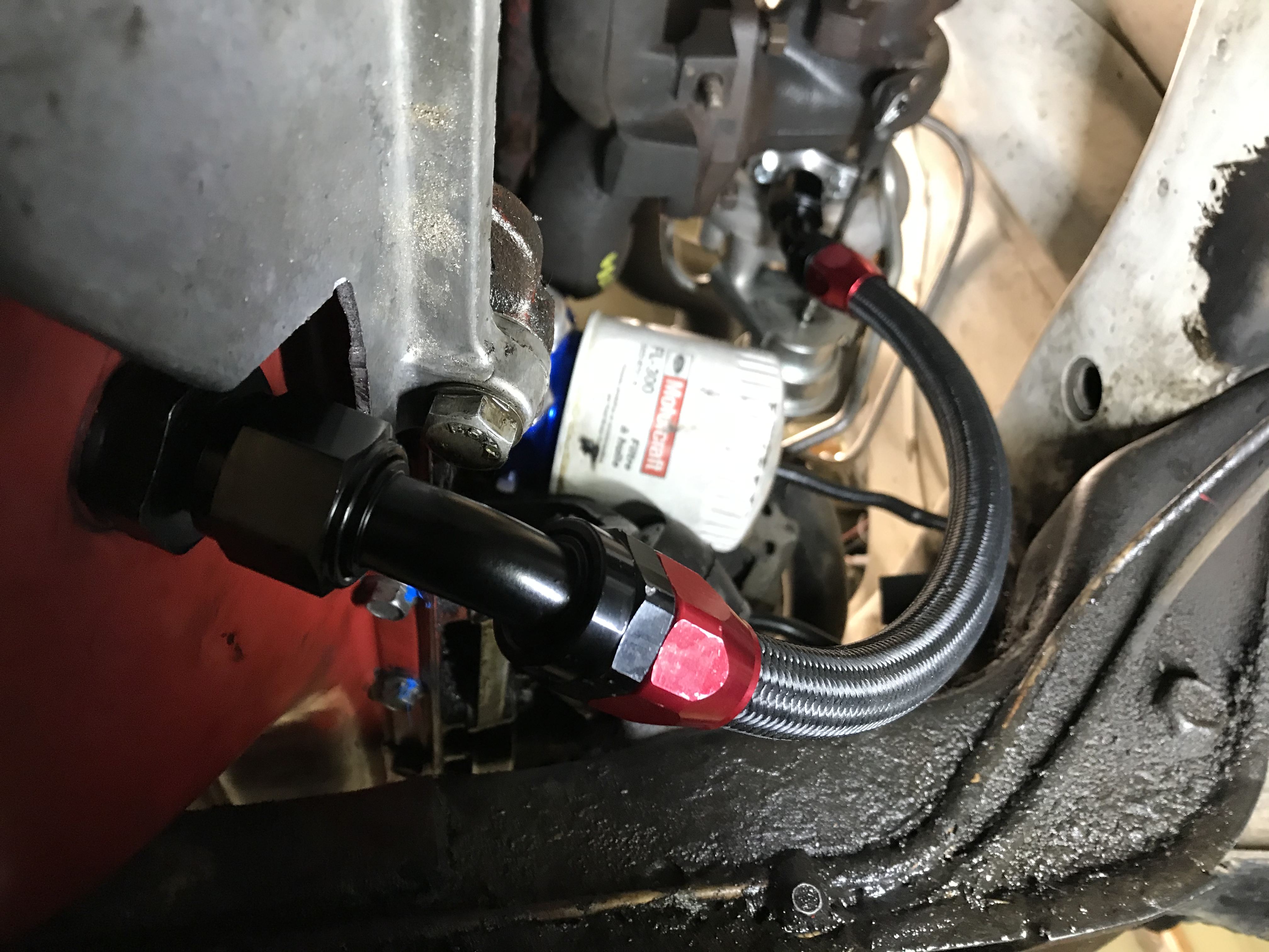 Black braided hose with red fittings going from a turbo to an oil pan
