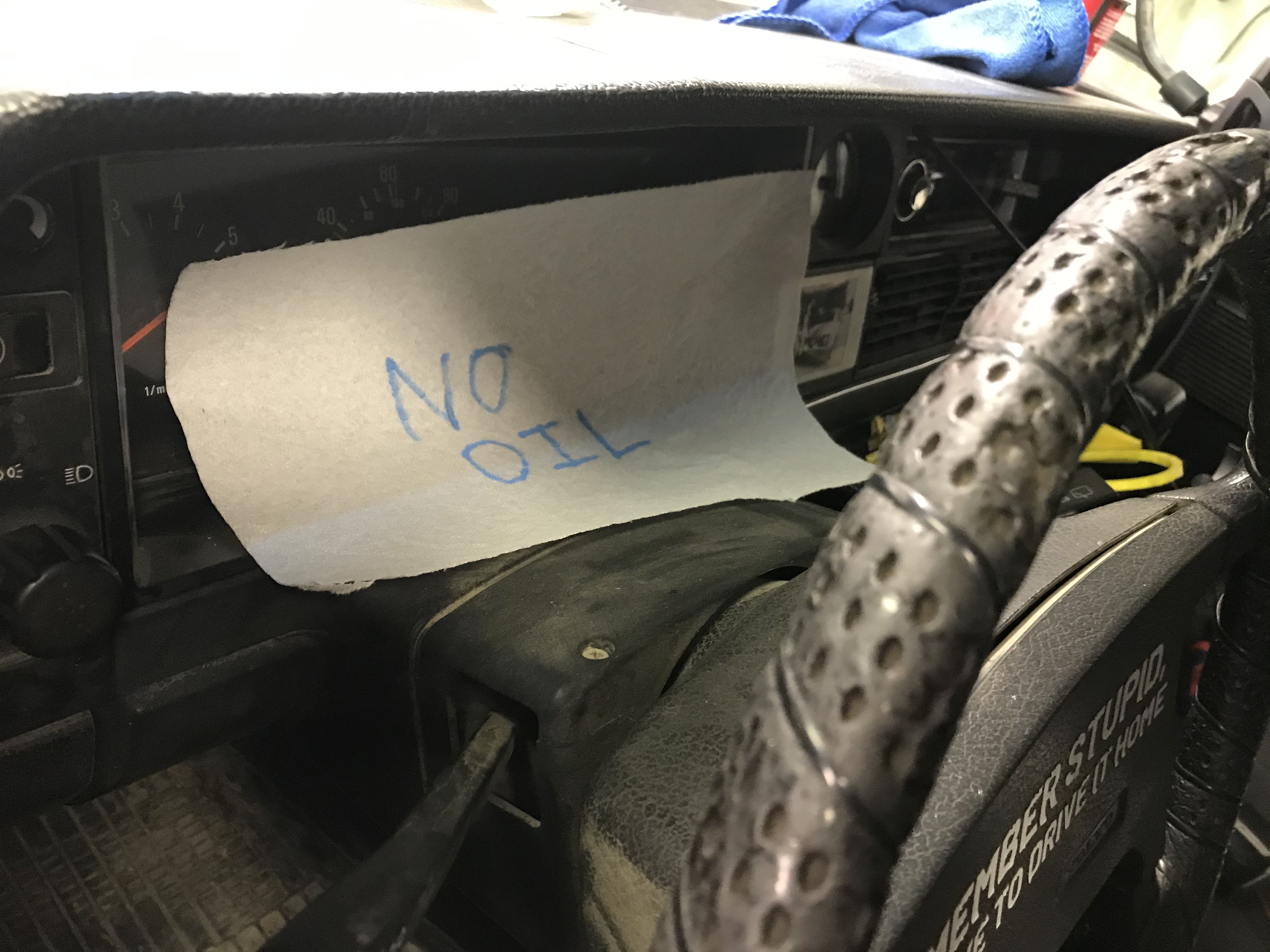 A paper towel draped over a car's instrument cluster with NO OIL written in black pen