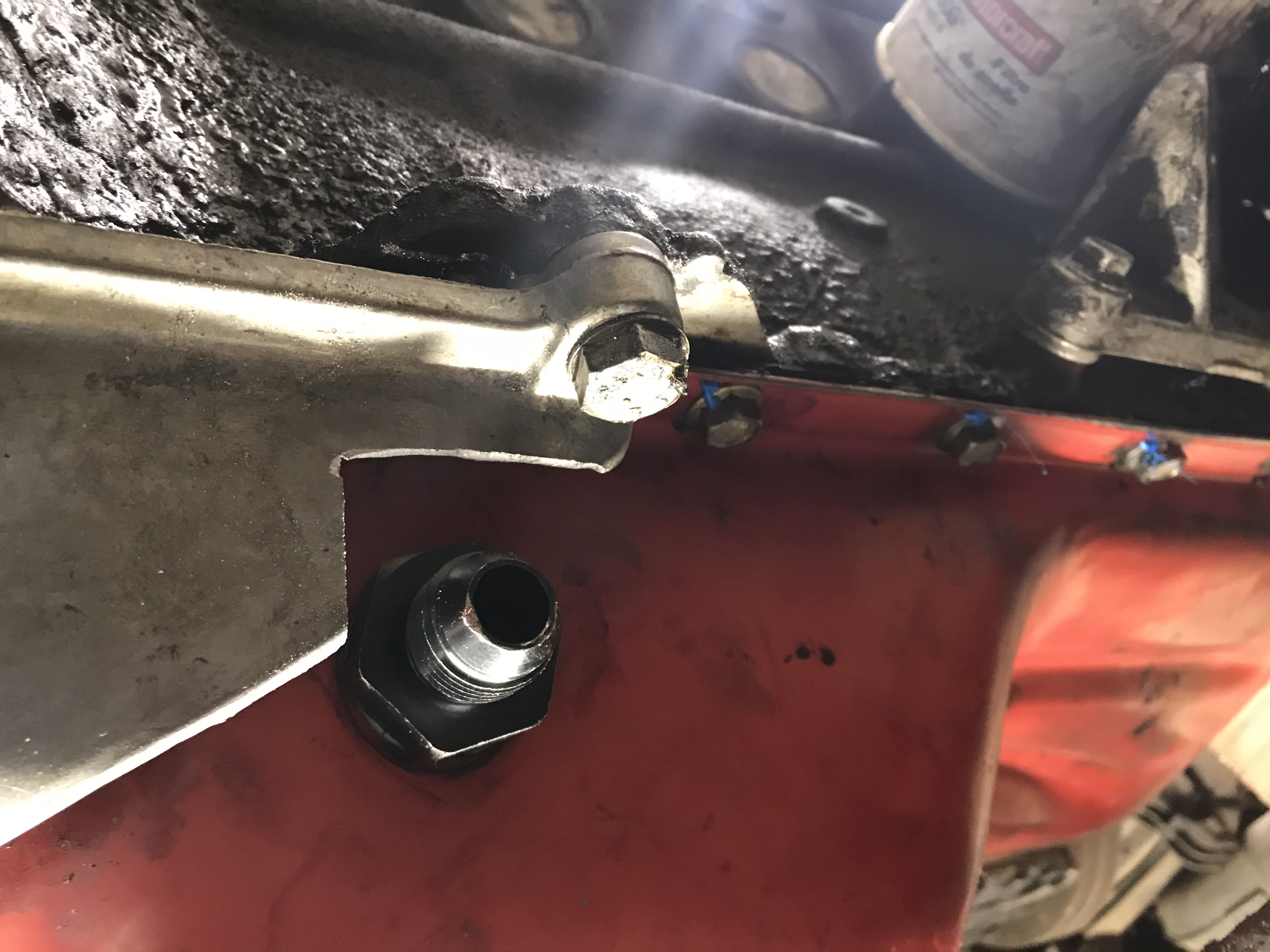 Fitting installed in the red oil pan with a roughly cut aluminum sheet in the foreground