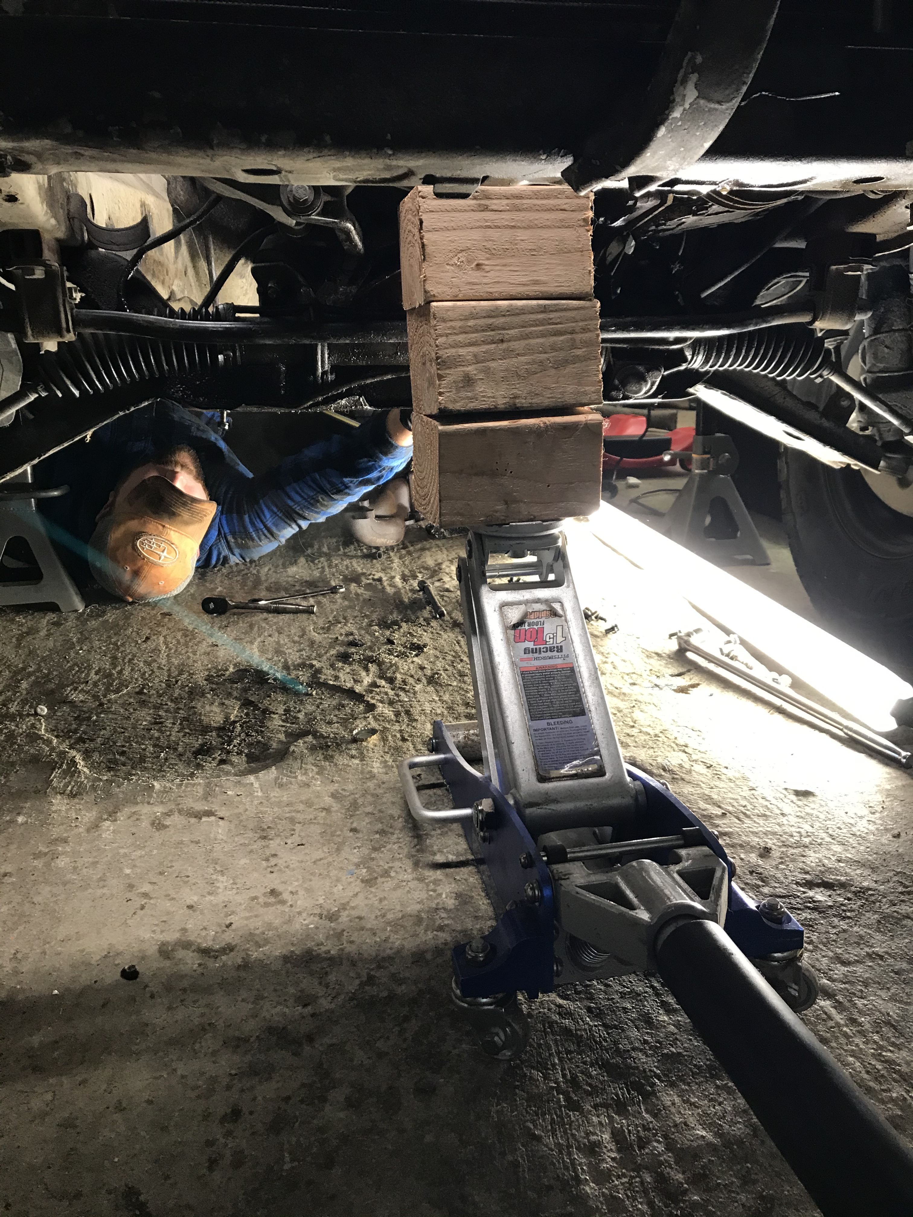 Engine pulley held up by floor jack and 3 unstable looking 4x4 blocks of plywood